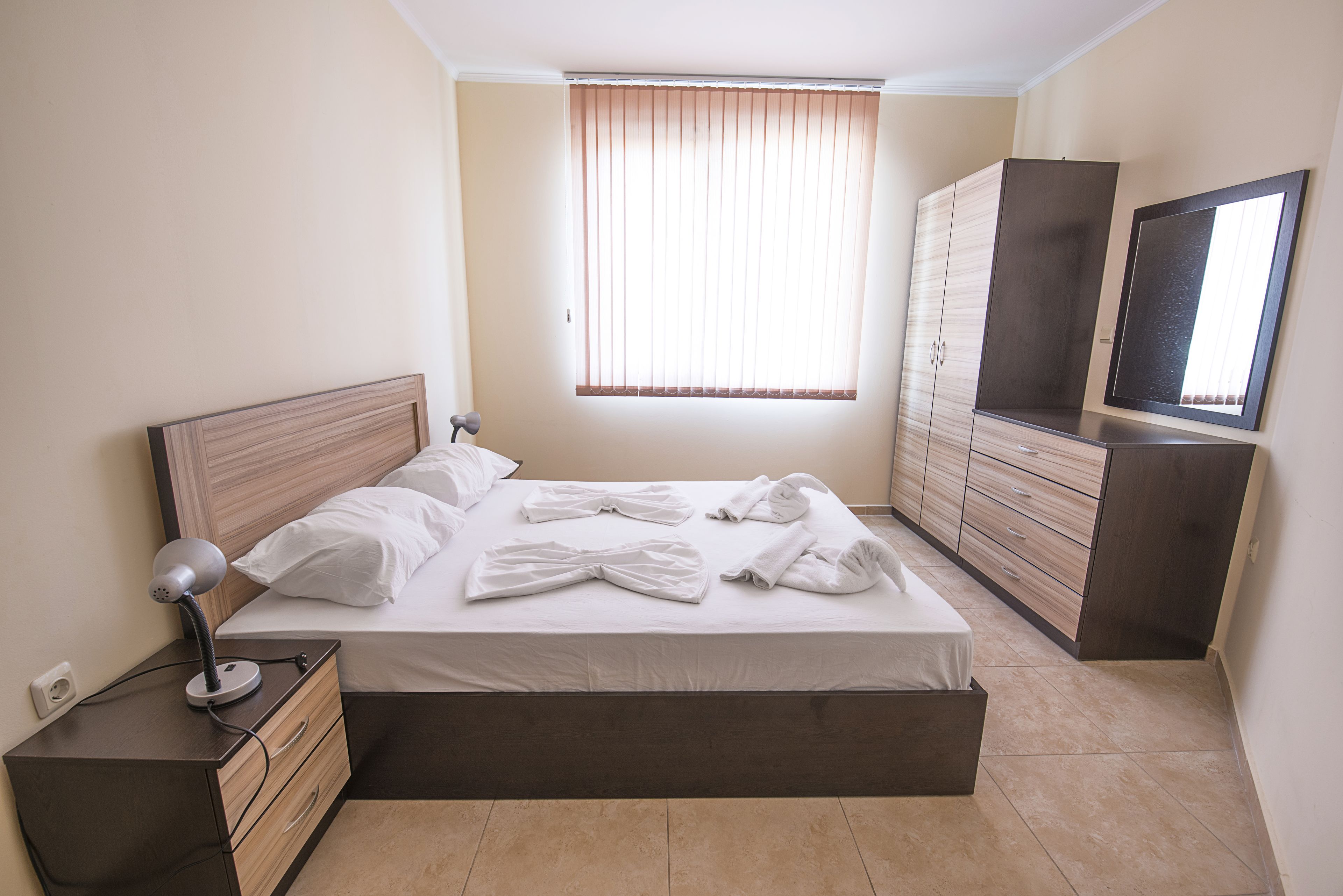 A neatly made bed with white linens, a bedside lamp, and a dresser with drawers.