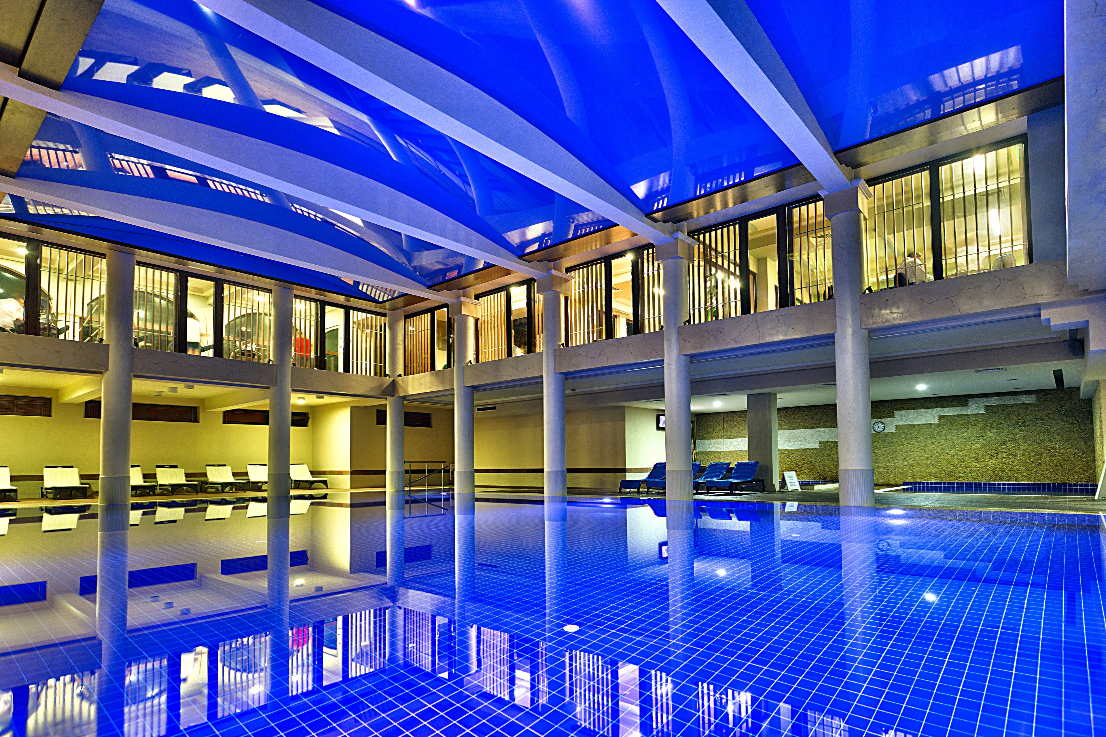 Una piscina interior con suelo de baldosas azules y un diseño arquitectónico moderno, que incluye un techo alto y ventanas amplias.