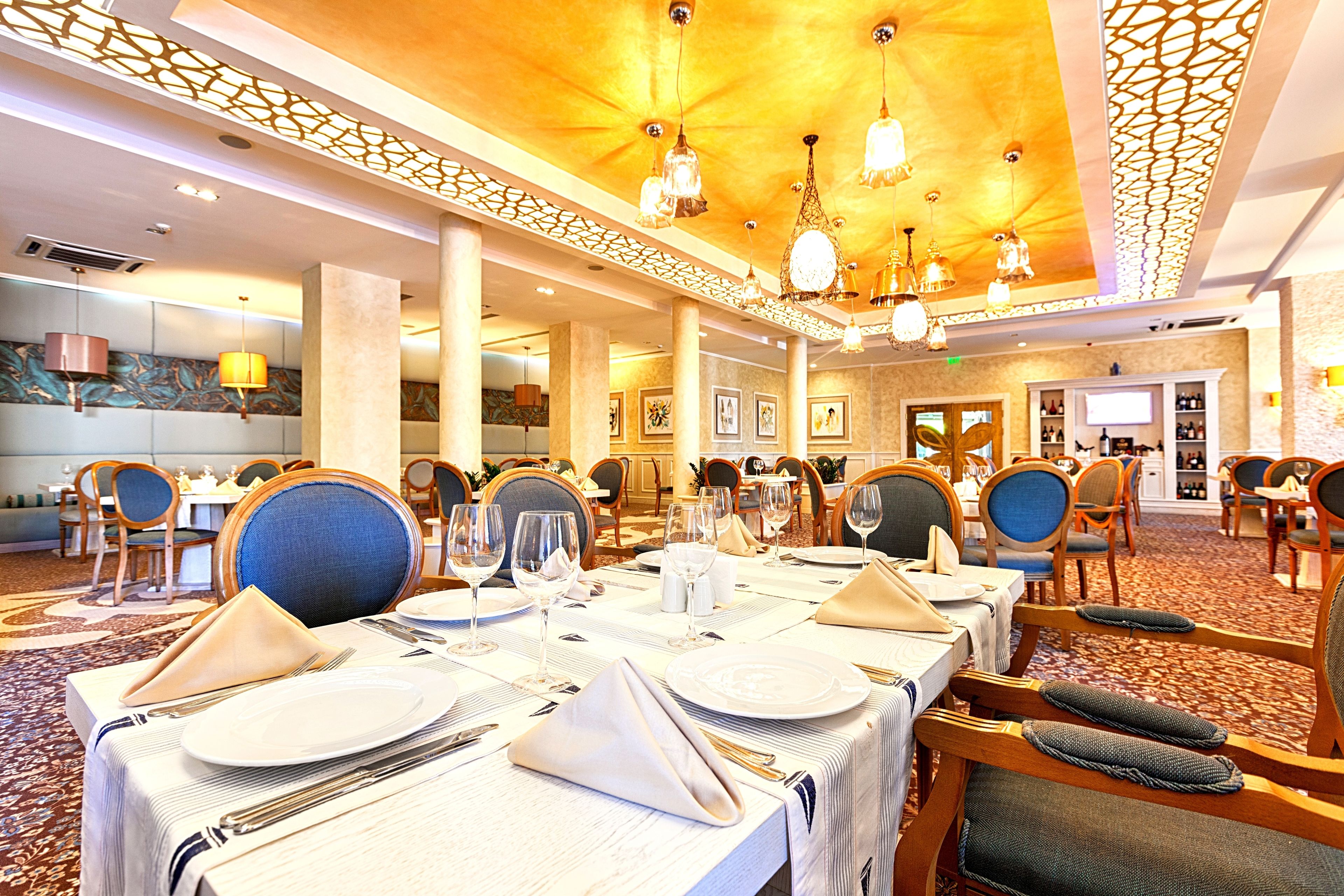 A well-lit dining area with tables set for service, featuring a patterned carpet and wooden chairs.