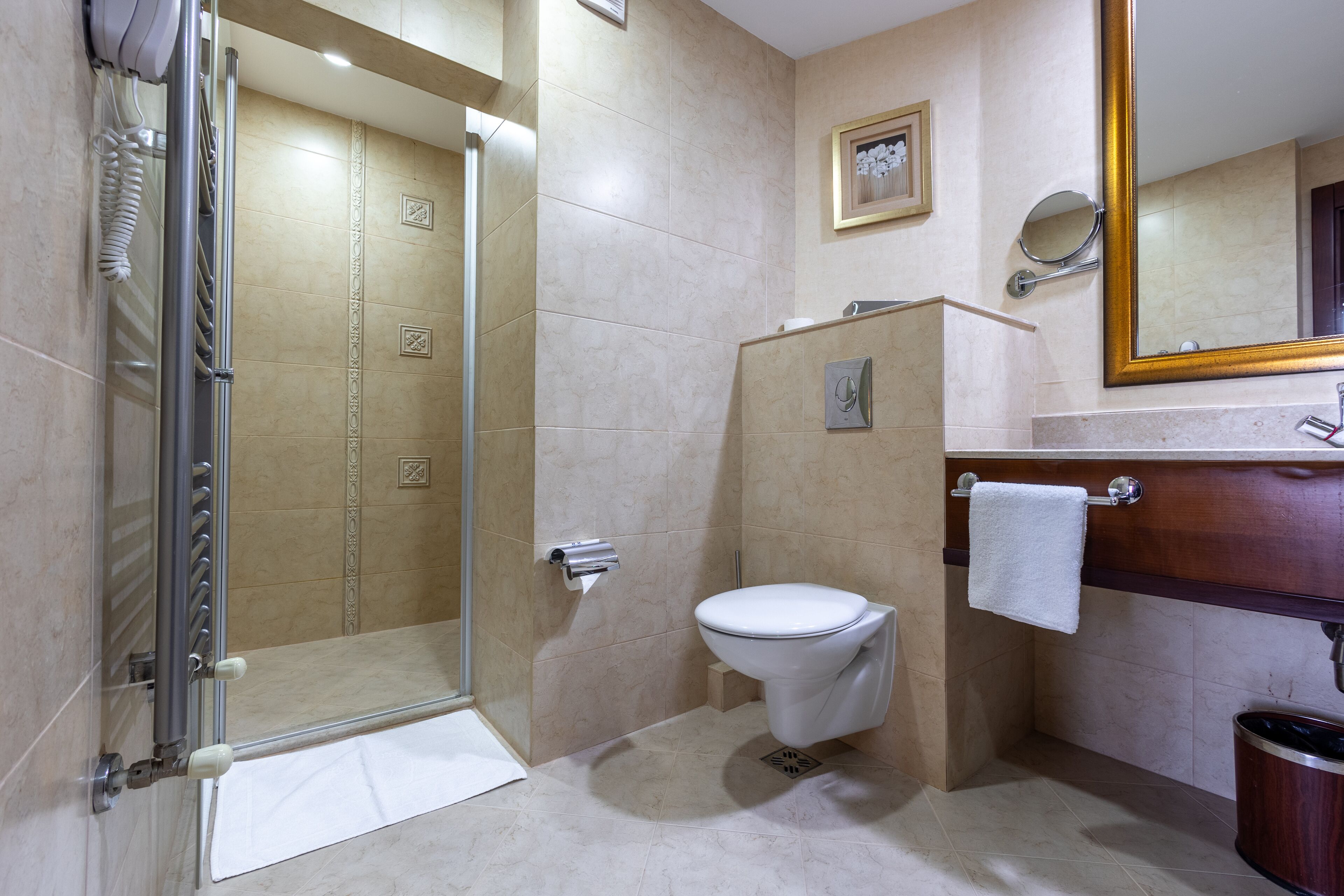 Un baño con cabina de ducha de vidrio, inodoro, lavamanos con espejo y toallero.