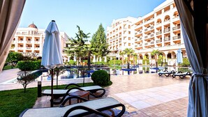 Um pátio de hotel com espreguiçadeiras, piscina e um edifício grande com várias varandas.