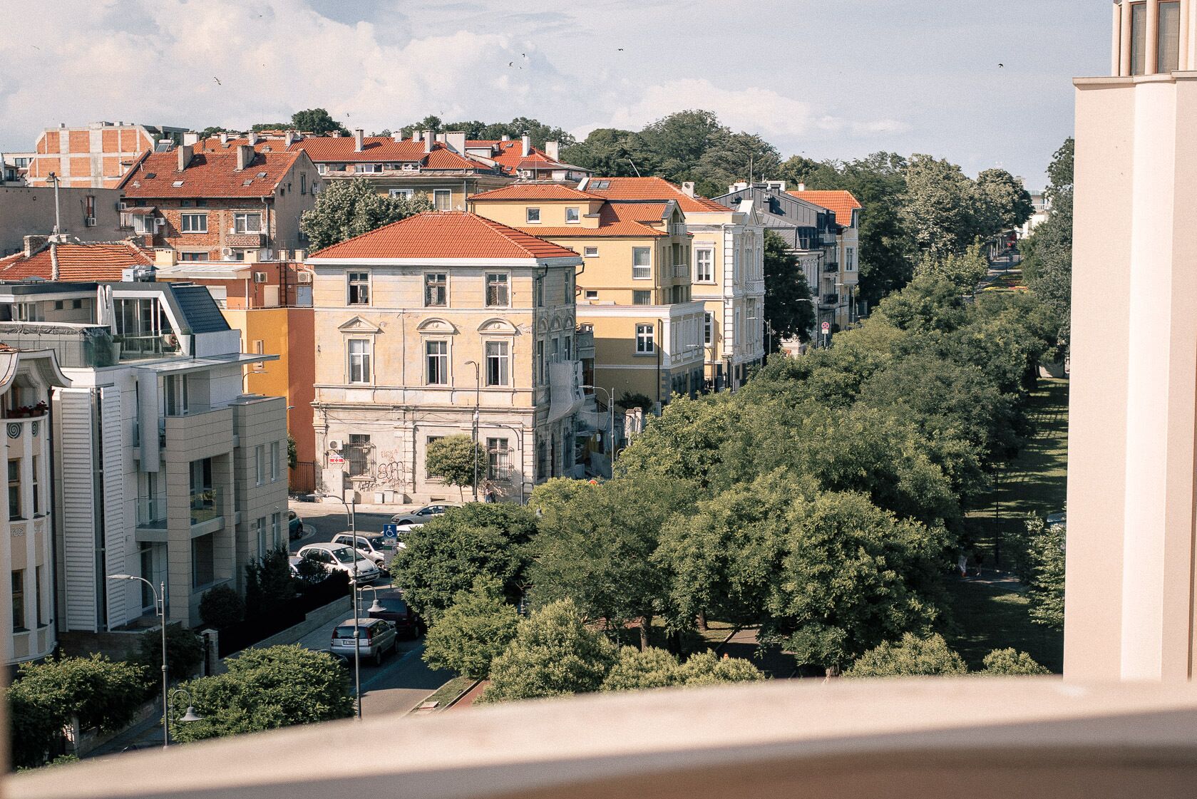 A cityscape with a mix of modern and traditional buildings, a clear sky, and a street with parked cars.