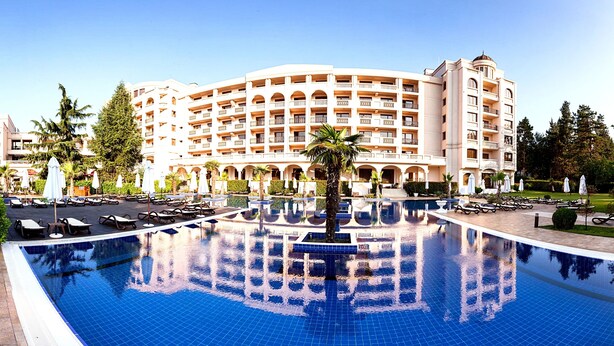 Um hotel grande com piscina central, várias varandas e paisagismo exuberante.