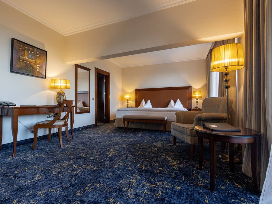 Une chambre d’hôtel comprenant un lit, deux tables de chevet avec des lampes, un bureau, une chaise et un sol recouvert de moquette.