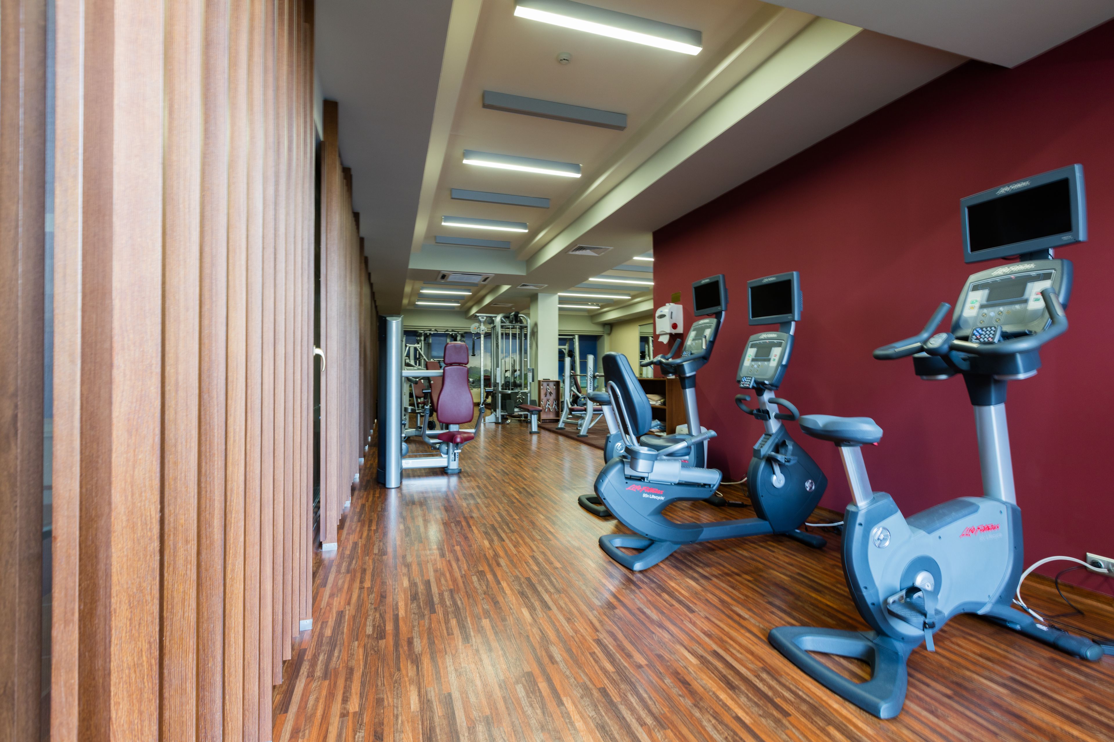 A gym with exercise equipment, wooden floors, and a red wall.