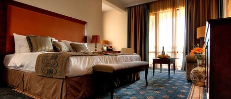 A hotel room with a large bed, a bench, a small table, a vase with flowers, and a lamp.