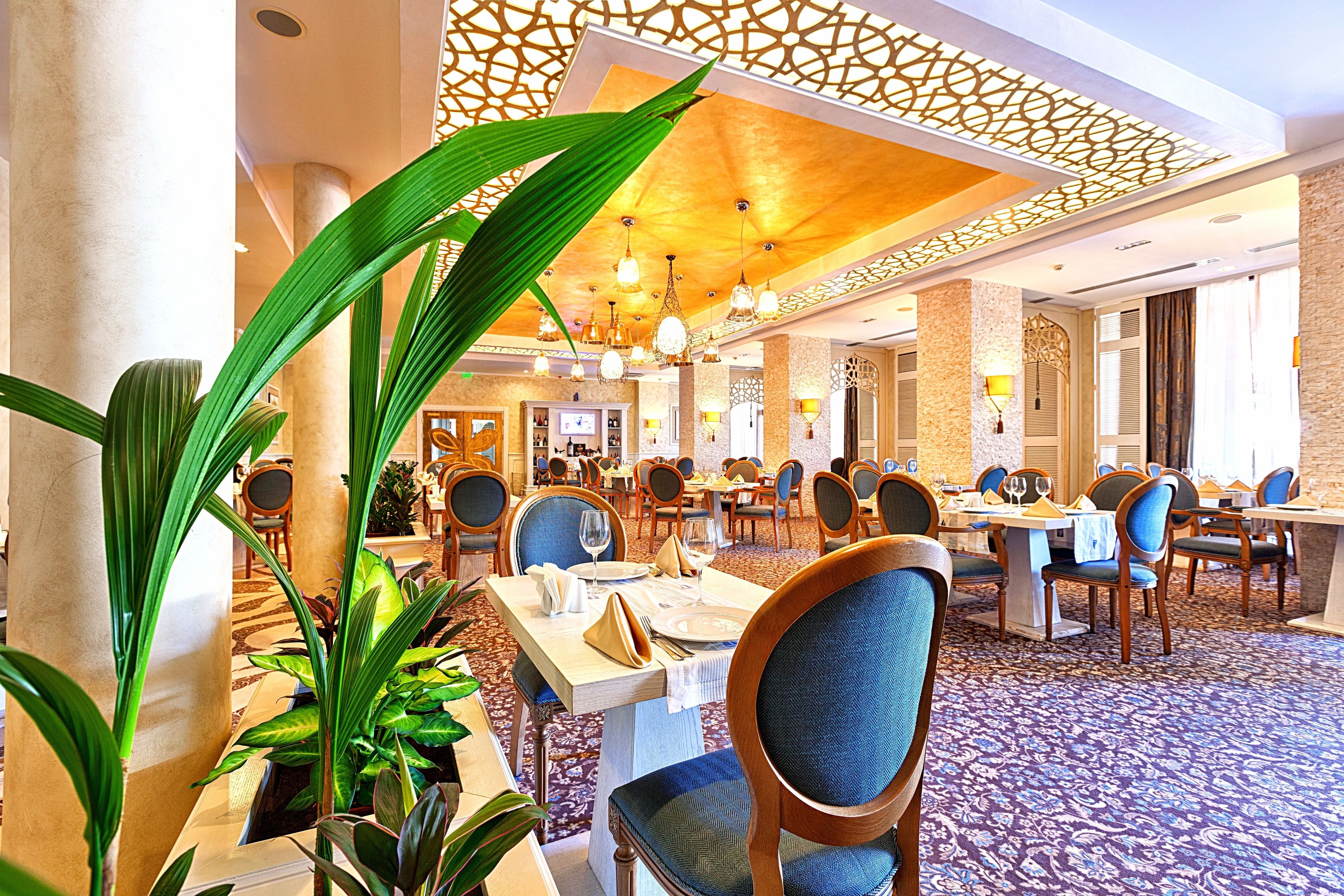 Une salle à manger d’hôtel avec plusieurs tables et chaises, un tapis à motifs et des panneaux décoratifs au plafond.