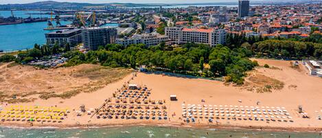 Vue aérienne d’une ville côtière avec une plage, des bâtiments et un port.
