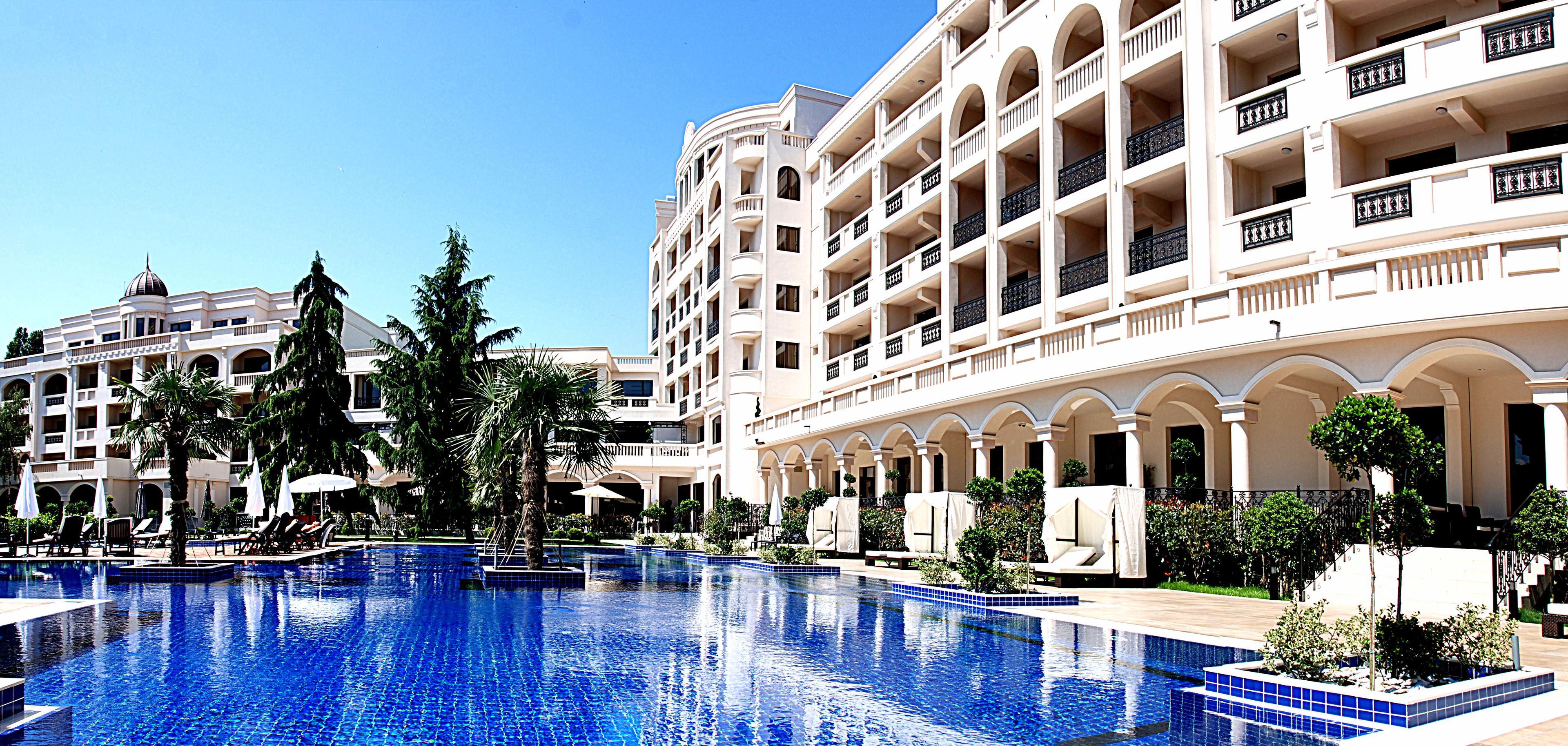 Un hotel con una piscina grande, varios balcones y jardines exuberantes.