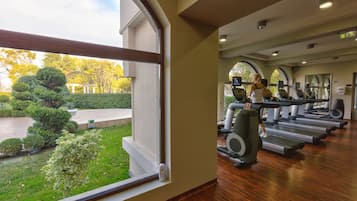 A gym with treadmills and exercise equipment, large windows with a view of a garden and trees.
