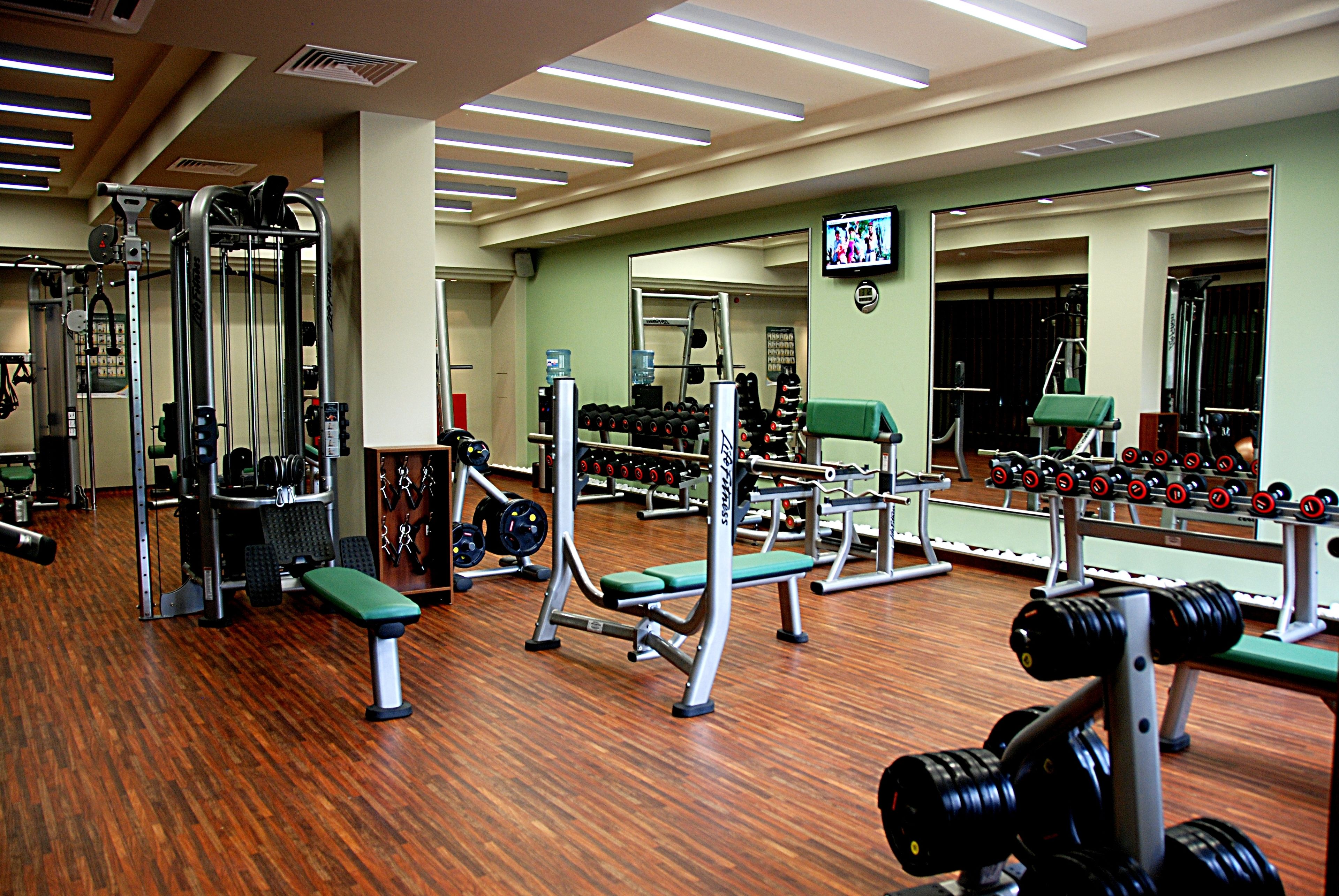 A gym with various exercise equipment, mirrors, and a television on the wall.