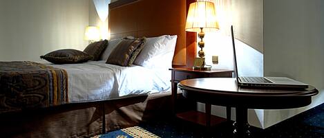 A hotel room with a bed, a desk with a laptop, and a lamp.