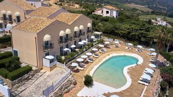 Un resort con una piscina grande, camas solárium y una cerca blanca que delimita el área.