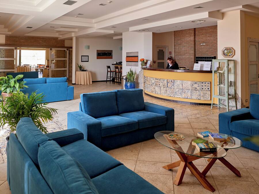 A spacious lobby with blue sofas, a reception desk, and a tiled wall.