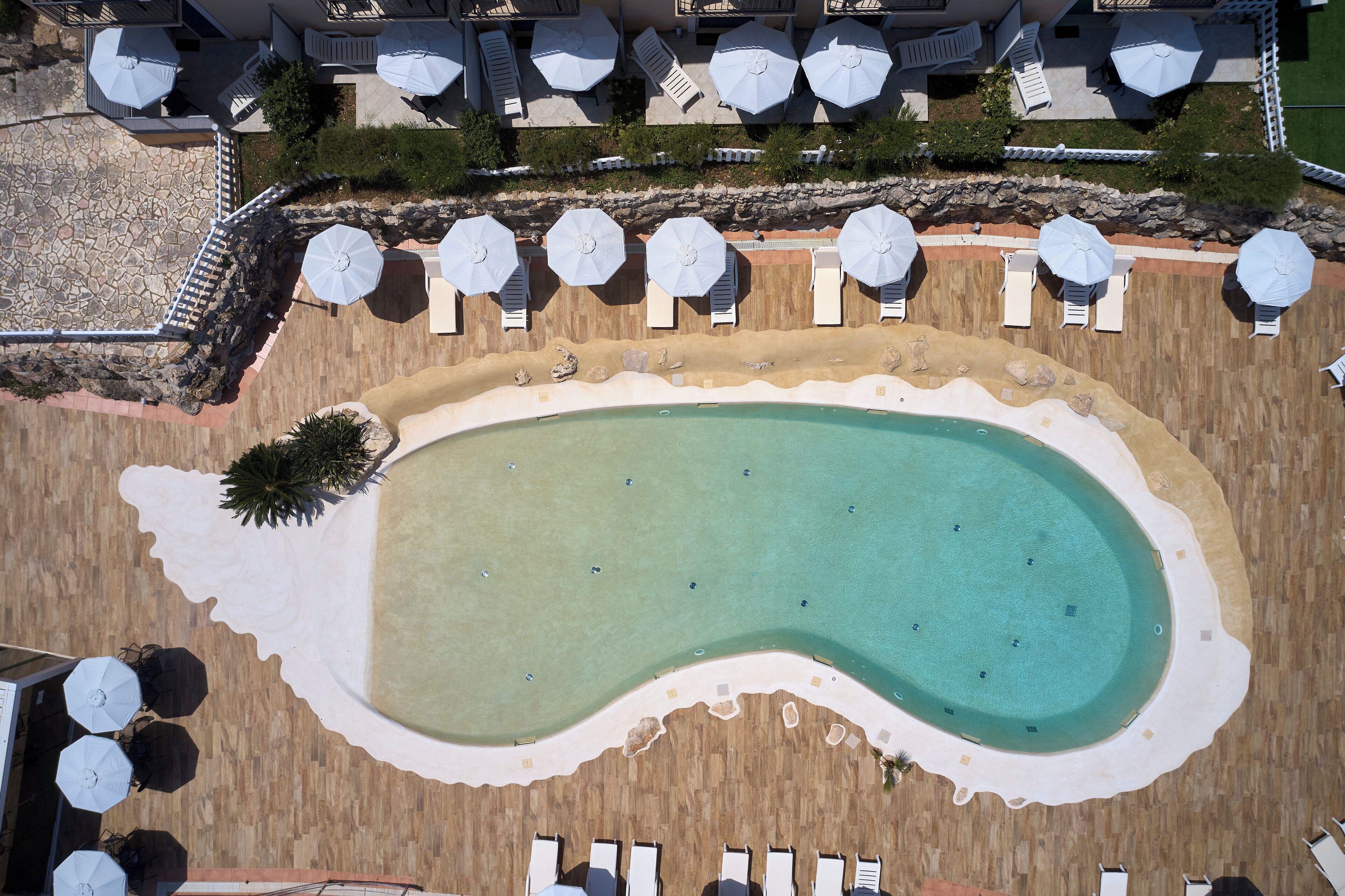 An aerial view of a resort with a large pool, sun loungers, and umbrellas.