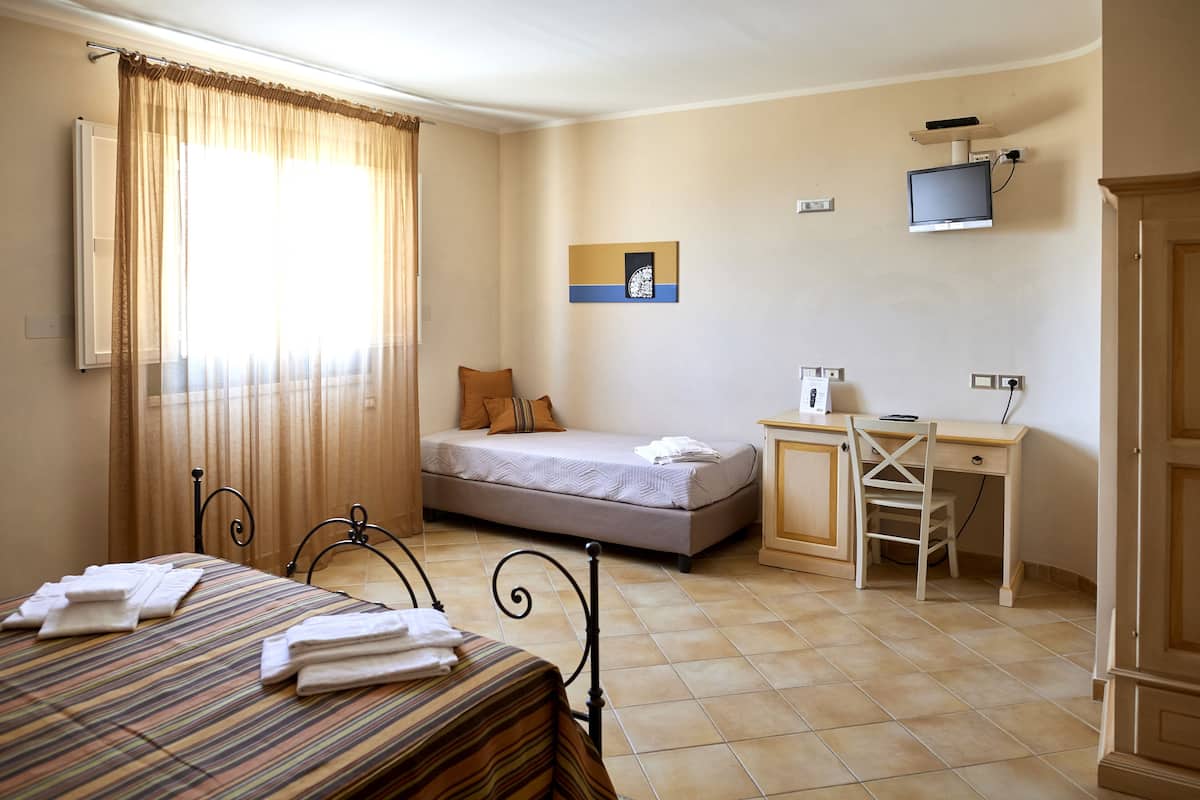 Una habitación de hotel con cama, escritorio, silla, televisor y ventana con cortinas.