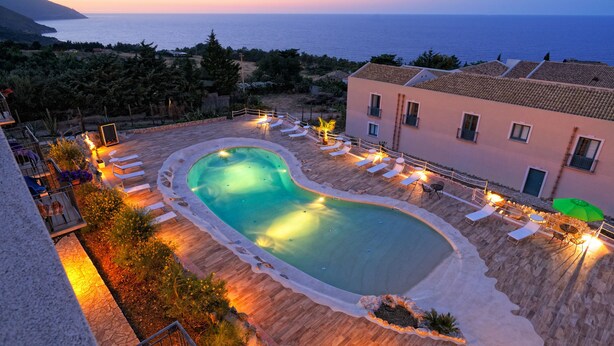 A swimming pool with lounge chairs and a view of the sea at dusk. - Baglio dello Zingaro (Castellammare del Golfo)
