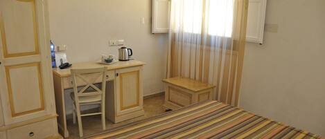 A hotel room with a bed, a desk with a chair, a small table, a television mounted on the wall, and a window with curtains.