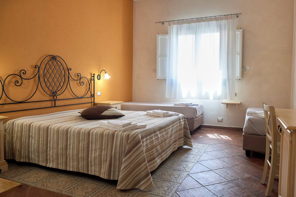 Un dormitorio con cama, mesita de noche y ventana con cortinas.