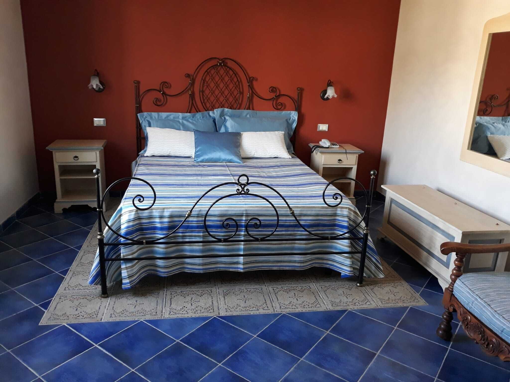 Un letto con struttura in metallo, una coperta a righe blu e bianche e due comodini con lampade.