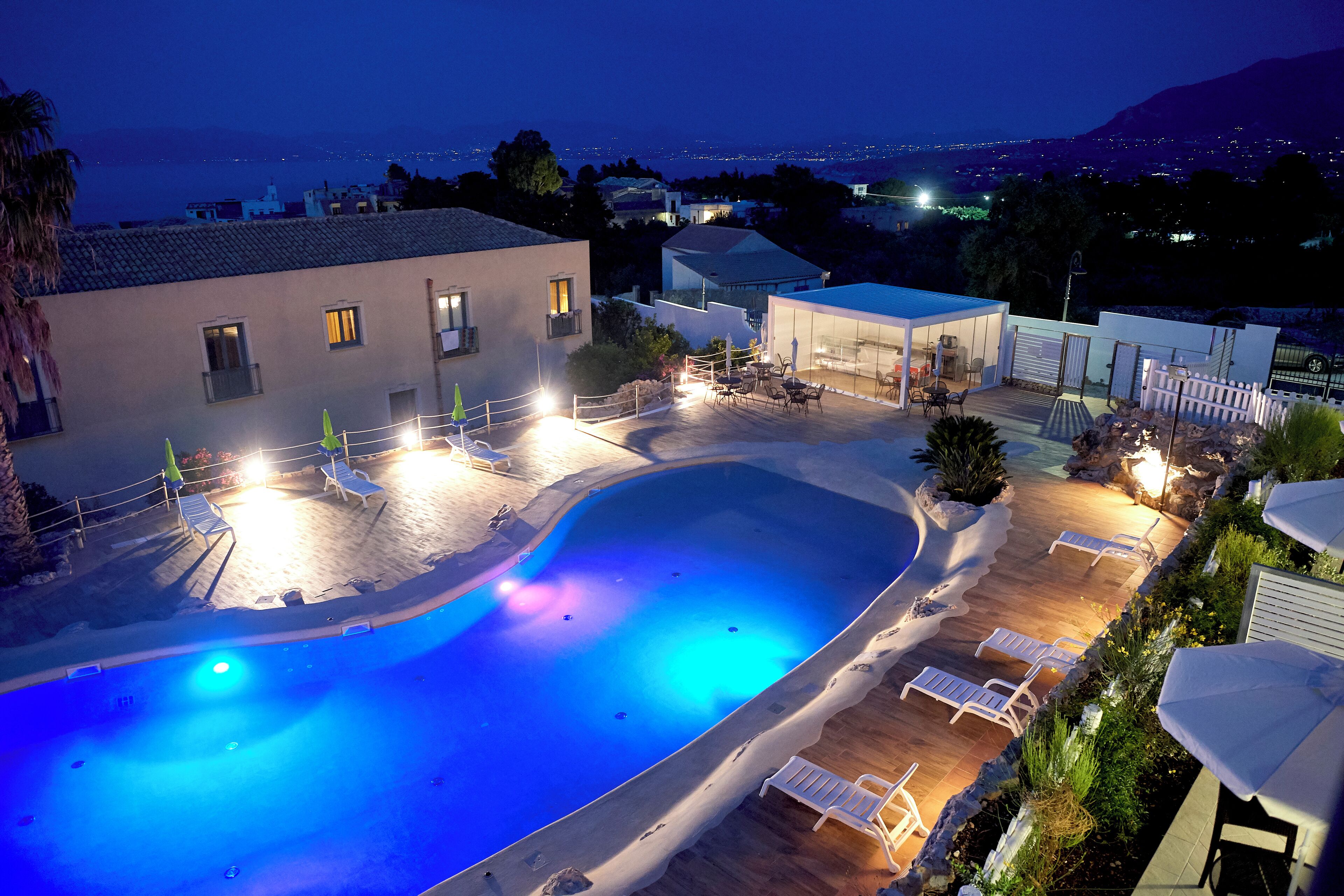 A swimming pool with lounge chairs and a view of the city at night.