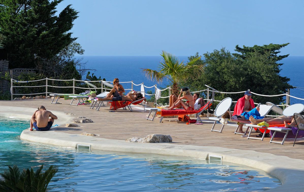 Un área junto a la piscina con sillones de descanso y vista al mar.