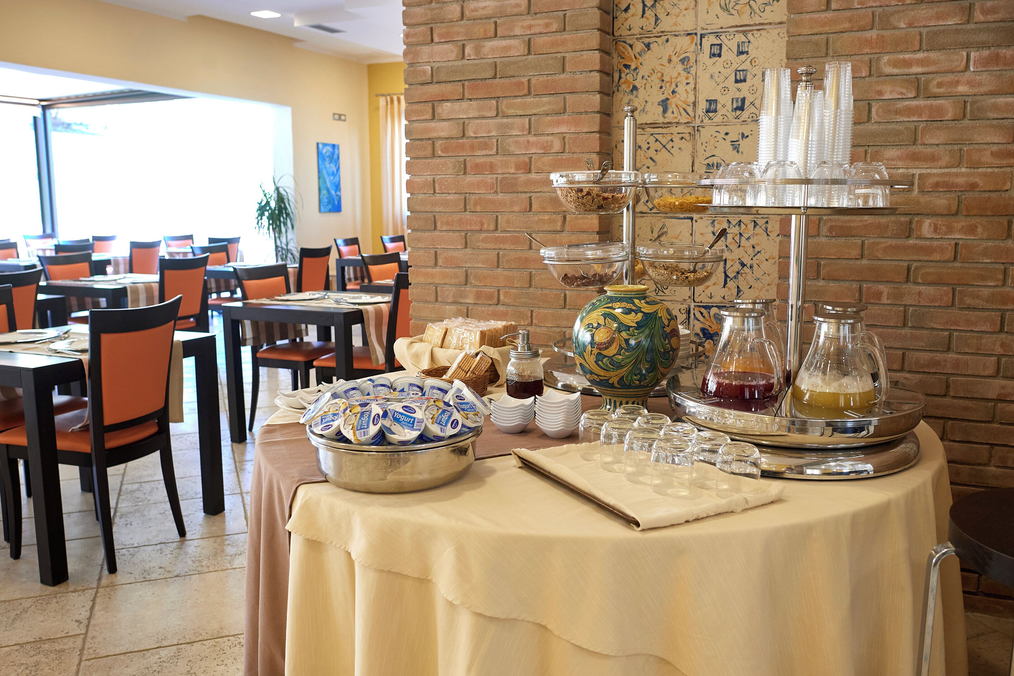 A buffet setup with various food items and beverages, including a bowl of yogurt, a tray of bread, and a tiered drink dispenser.