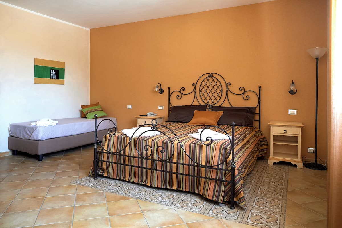 Un dormitorio con una cama, un sofá más pequeño, una mesita de noche, una lámpara y un cuadro colgado en la pared.