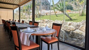 A restaurant with tables set for dining, large windows offering a view of a rocky landscape and greenery. - Baglio dello Zingaro (Castellammare del Golfo)