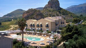 A hotel with a pool, outdoor seating, and a view of a mountain. - Baglio dello Zingaro (Castellammare del Golfo)