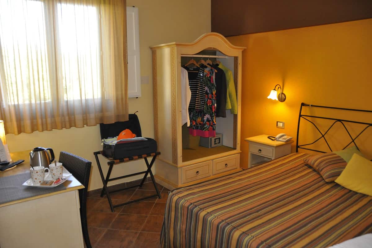 Habitación de hotel con una cama, un escritorio con hervidor y tazas, un armario, una lámpara de noche y un teléfono.