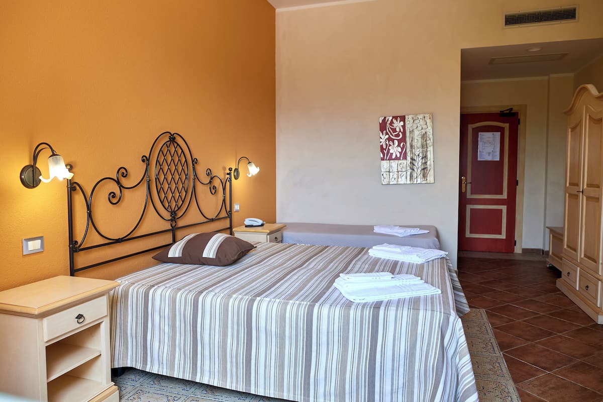 Una habitación de hotel con cama, mesitas de noche, lámpara de pared y una puerta con marco rojo.