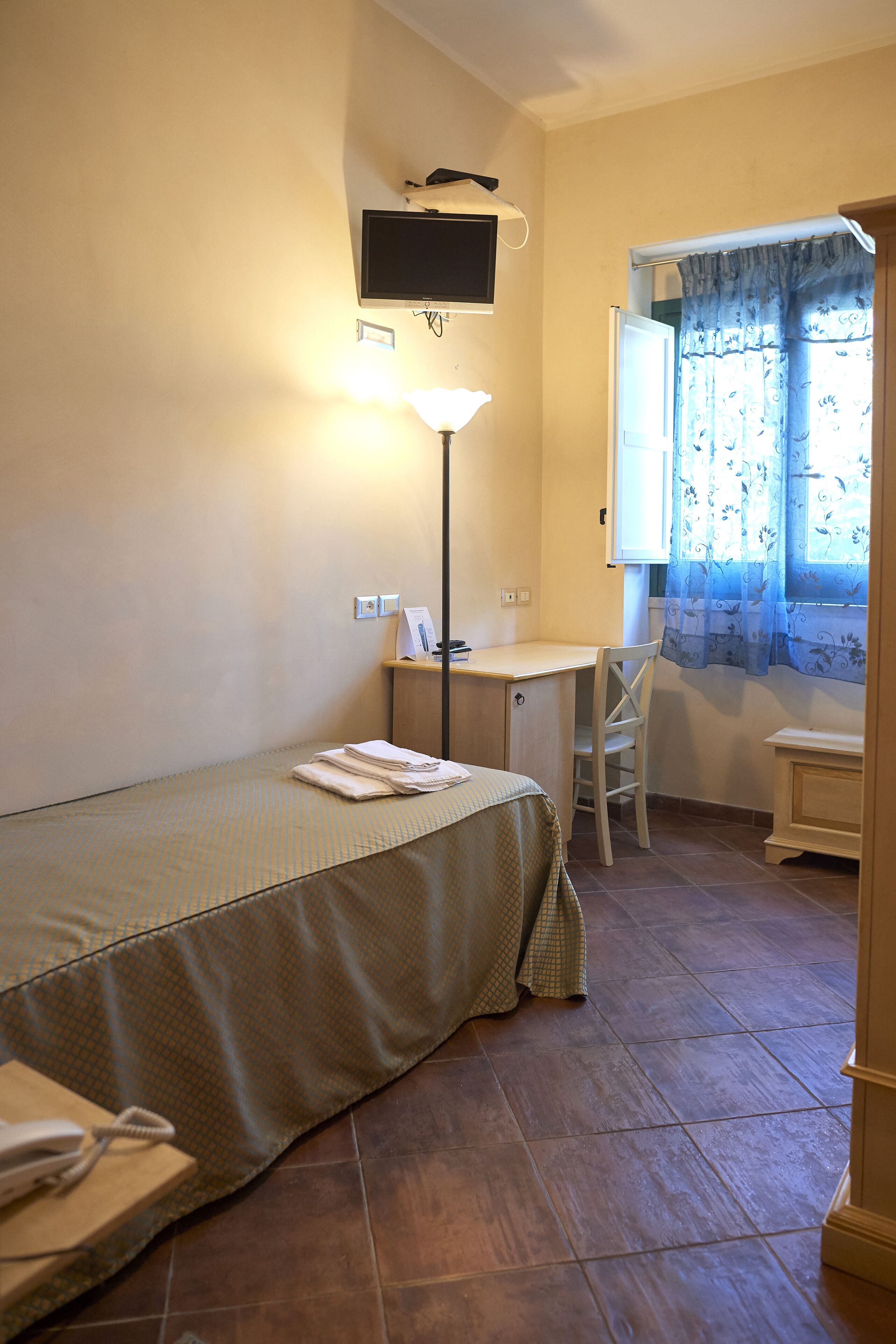 A small, neatly arranged room with a bed, a desk, a chair, and a television mounted on the wall.