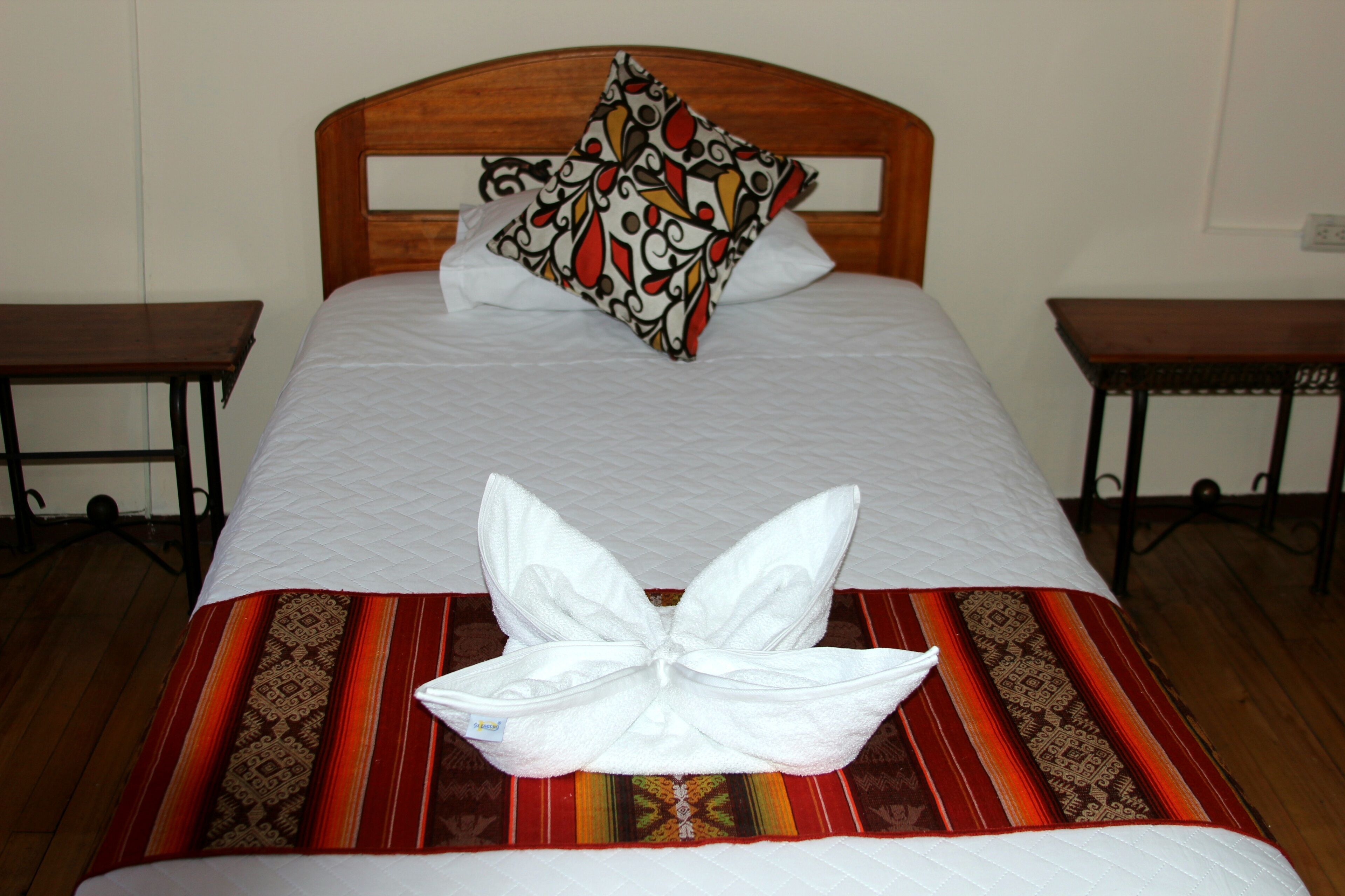 A neatly made bed with a floral pillow and a towel arranged in a bow shape.