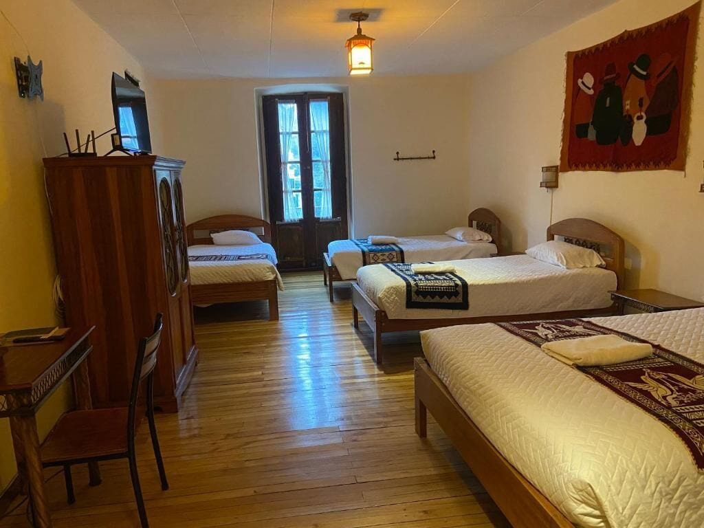 A hotel room with two beds, a wooden desk, a chair, and a wardrobe.