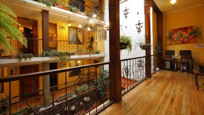 Un interior de varios niveles con pisos de madera, balcones con plantas y una araña.