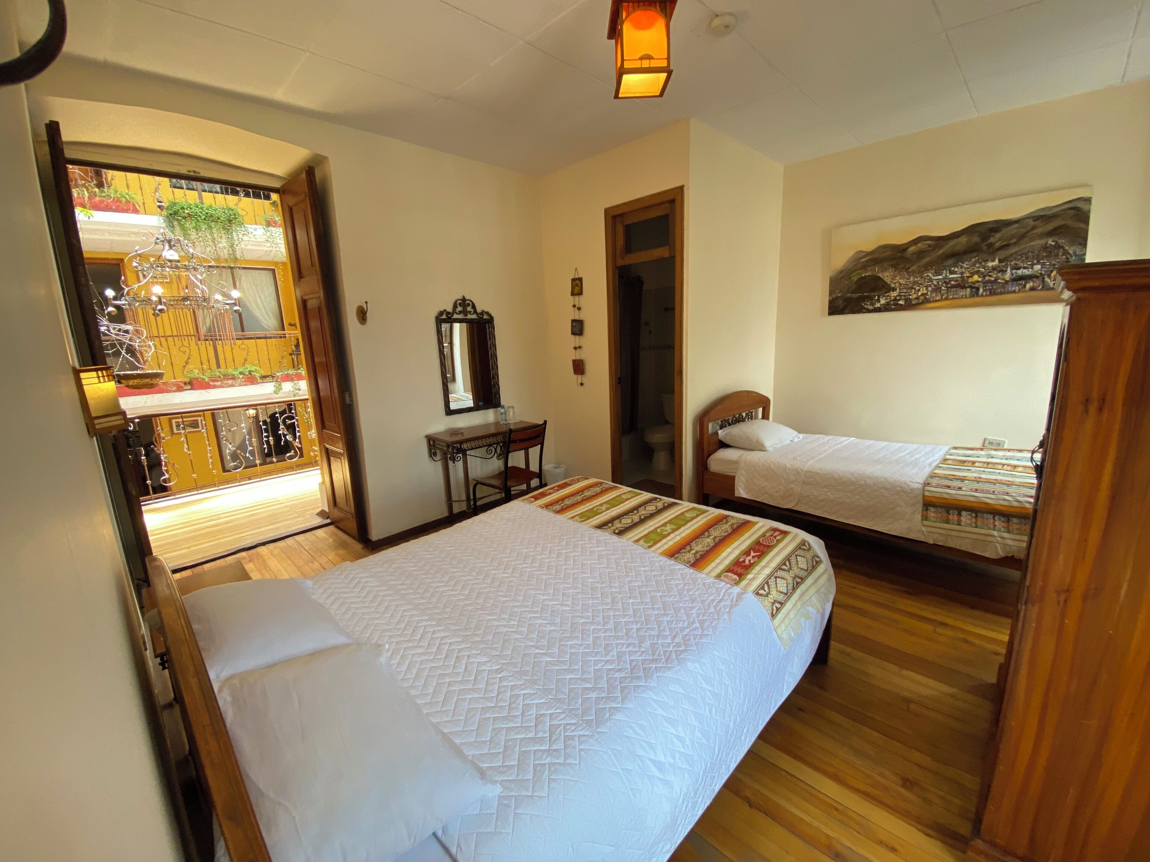 A bedroom with two beds, a wooden desk, a mirror, and a painting on the wall.