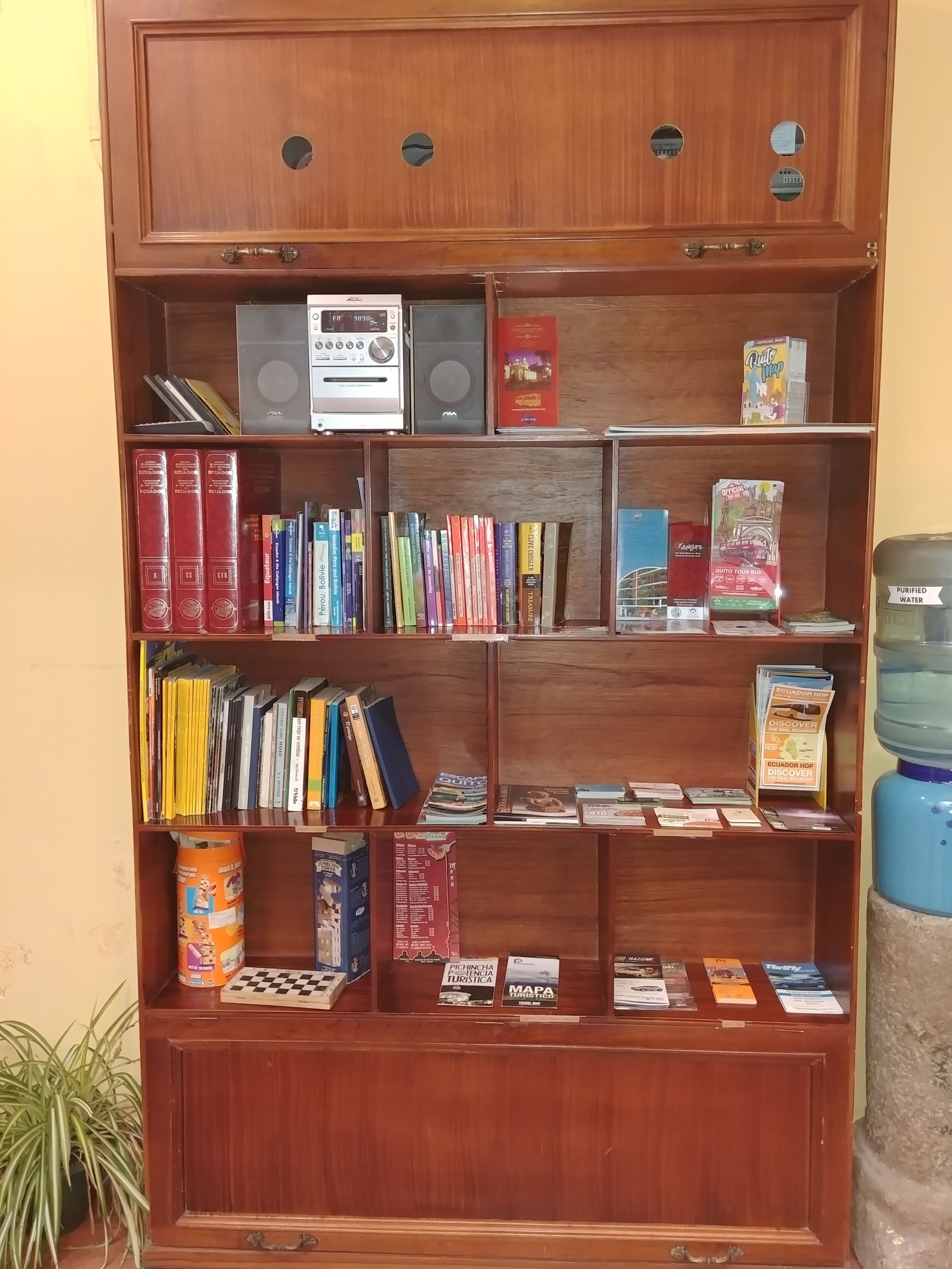 A wooden bookshelf with various travel books, maps, and a water dispenser.