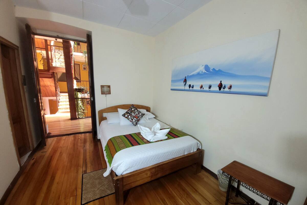 A hotel room with a wooden bed, a painting of a mountain landscape, and a small table.