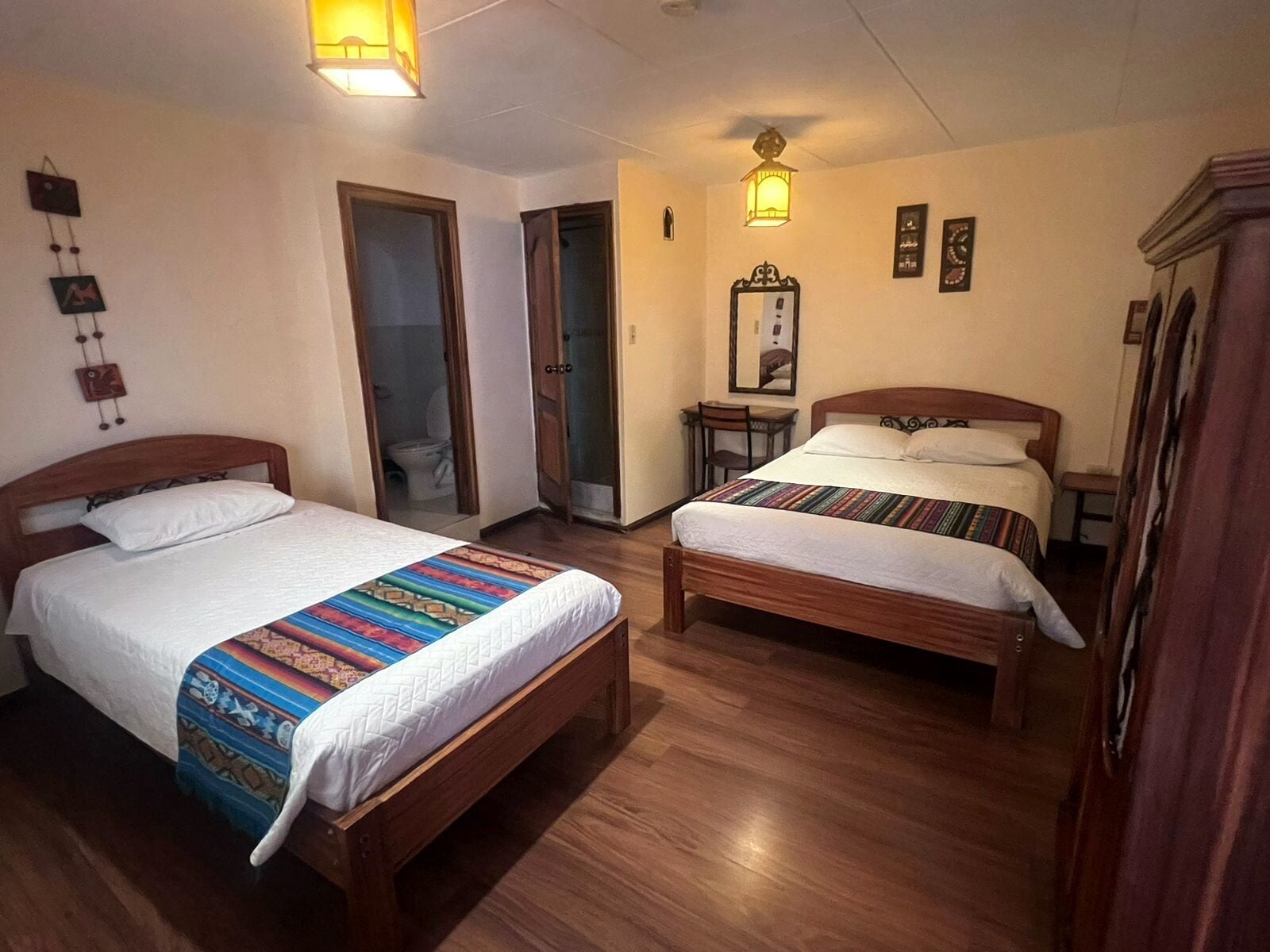 A room with two wooden beds, a small table, a chair, and a mirror on the wall.