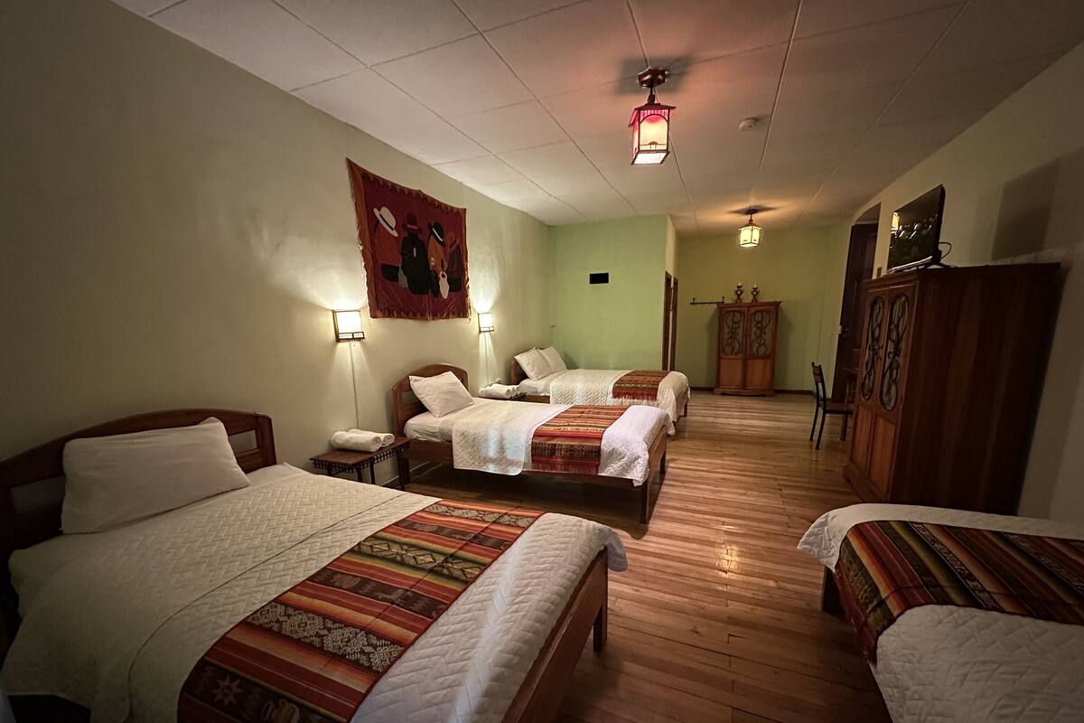 A hotel room with three beds, wooden floors, a tapestry on the wall, and a cabinet.