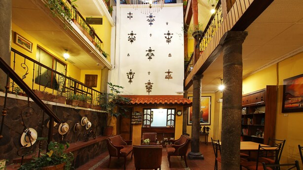 Un amplio atrio con techo alto, una zona de estar central con sillas y una mesa, y un balcón con plantas.