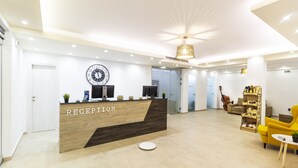 A reception area with a wooden desk labeled "RECEPTION," a clock, and a modern chandelier. - Hotel Odysseas (Kassandra)