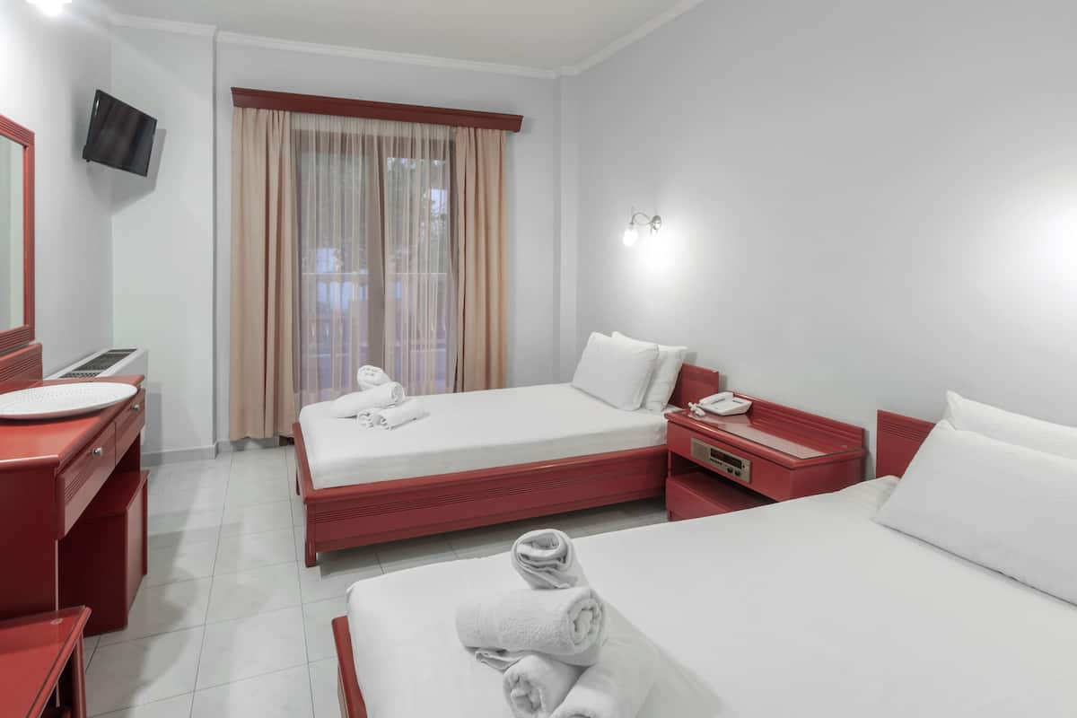 A hotel room with a bed, a desk with a computer, a TV mounted on the wall, and a window with curtains.