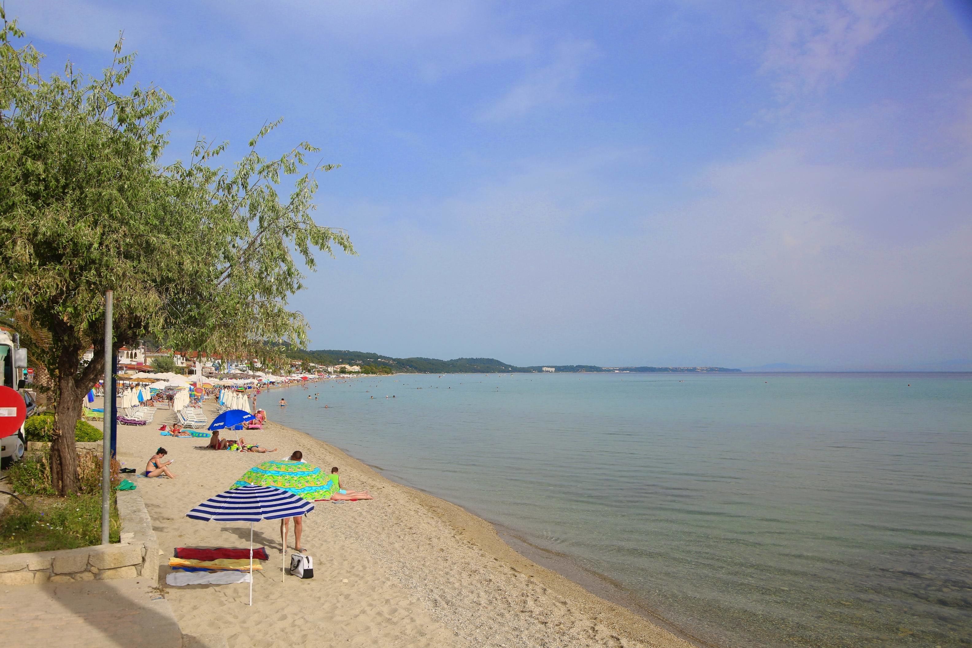 Une plage avec une eau claire, des parasols et des gens qui se détendent.