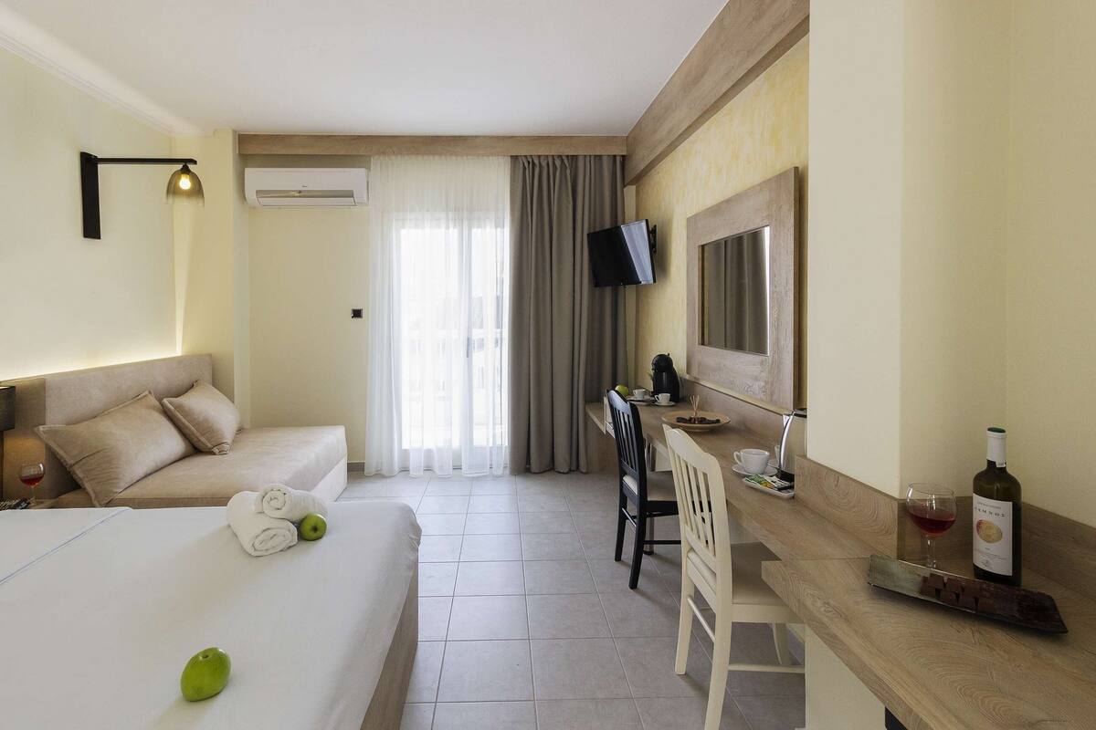 A hotel room with a bed, a desk, a television, and a bottle of wine.
