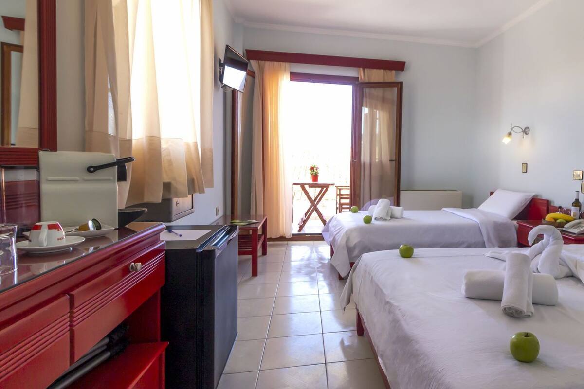 A hotel room with two beds, a desk, a TV, and a small balcony.
