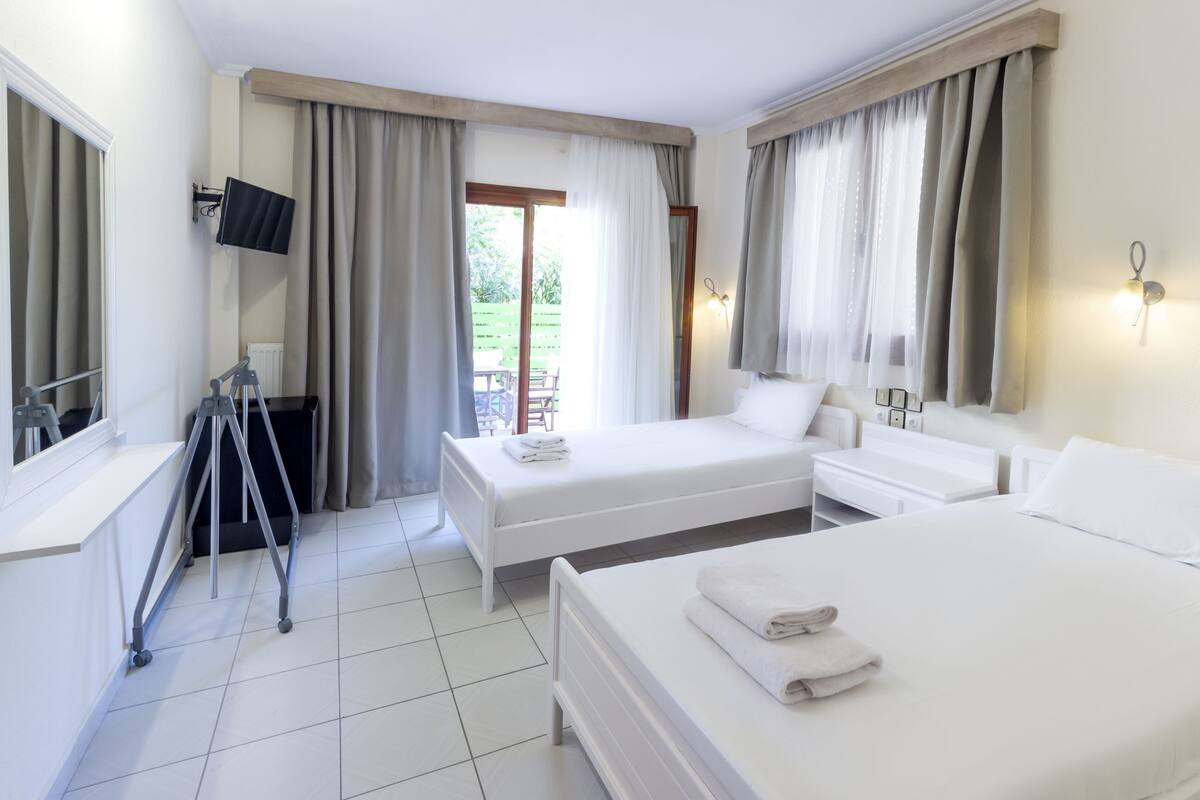 A hotel room with two beds, a TV, a desk, and a window with curtains.