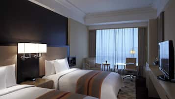 A hotel room with two beds, a desk, a television, and a window with curtains.