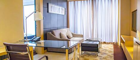 Una habitación de hotel moderna con un escritorio de vidrio, una silla de cuero, un sofá y un ventanal con cortinas.